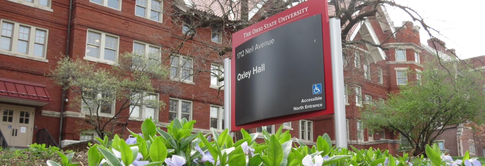 Oxley Hall sign, with building in background and spring flowers in foreground