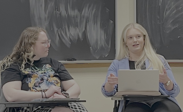 two alumni sitting in chairs, speaking to the students