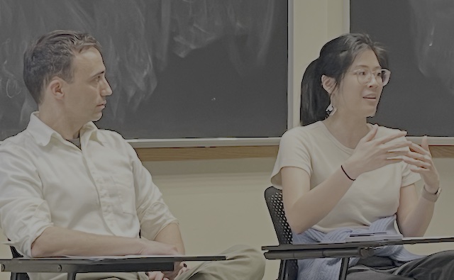 two guest speakers sitting in desks in front of the class