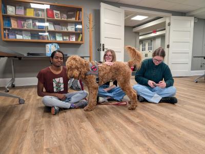 three students sitting on the floor, petting the dog
