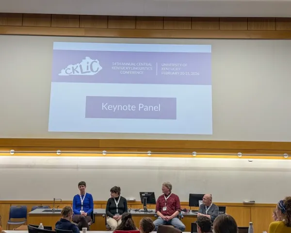 four panelists sitting in front of the crowd underneath a large screen