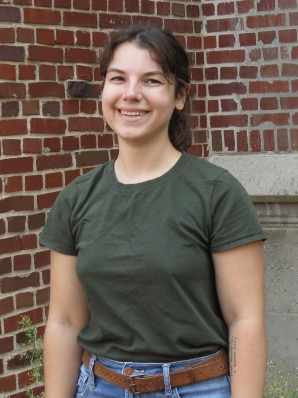 katie conner smiling at camera. Katie is wearing a green shirt and blue jeans, and has medium brown hair in a ponytail