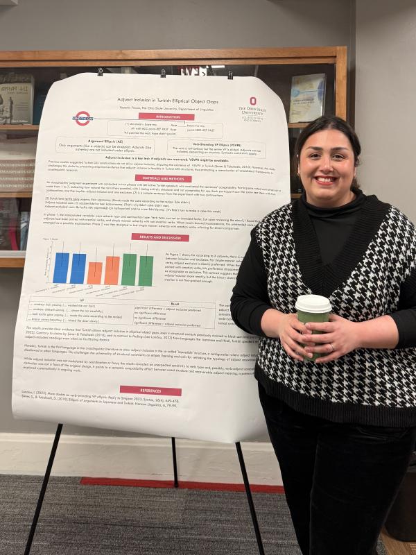Yasemin Fincan in front of her poster, holding a coffee cup