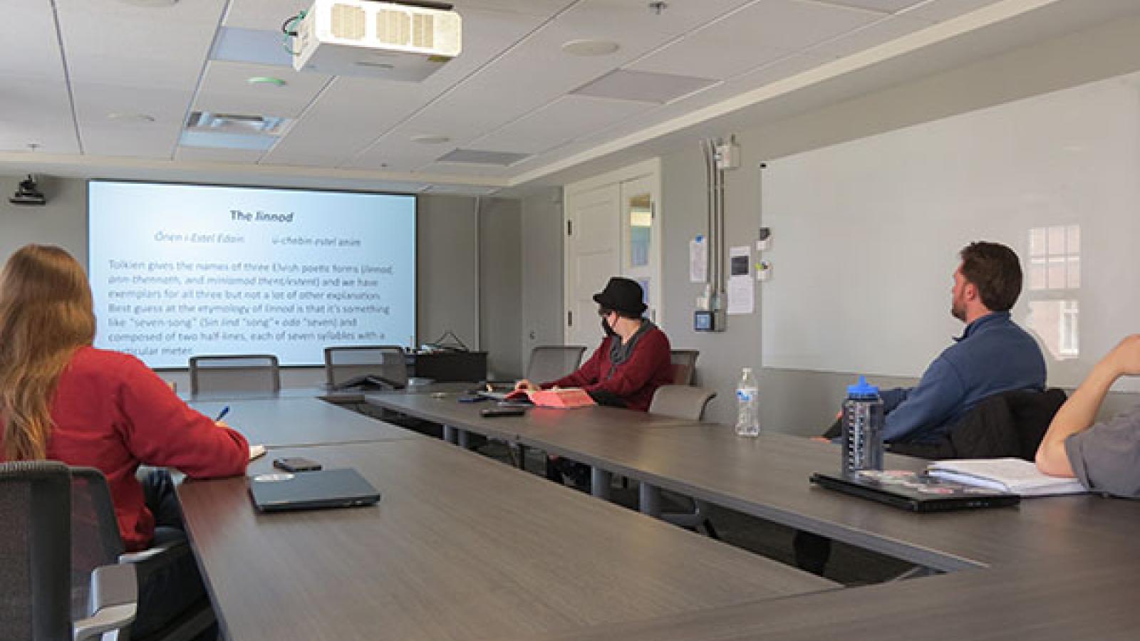 Julia Papke discusses Lord of the Rings material on the screen; they are sitting with students around the conference table