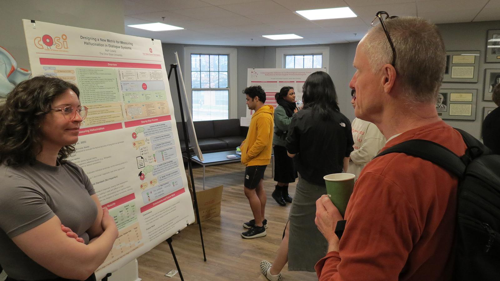 graduate student presenting a poster with a man, other posters and presenters in the background