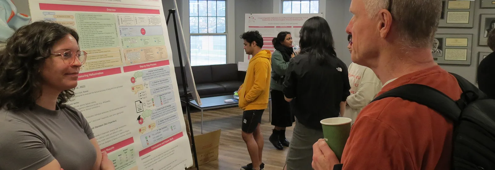 graduate student presenting a poster with a man, other posters and presenters in the background